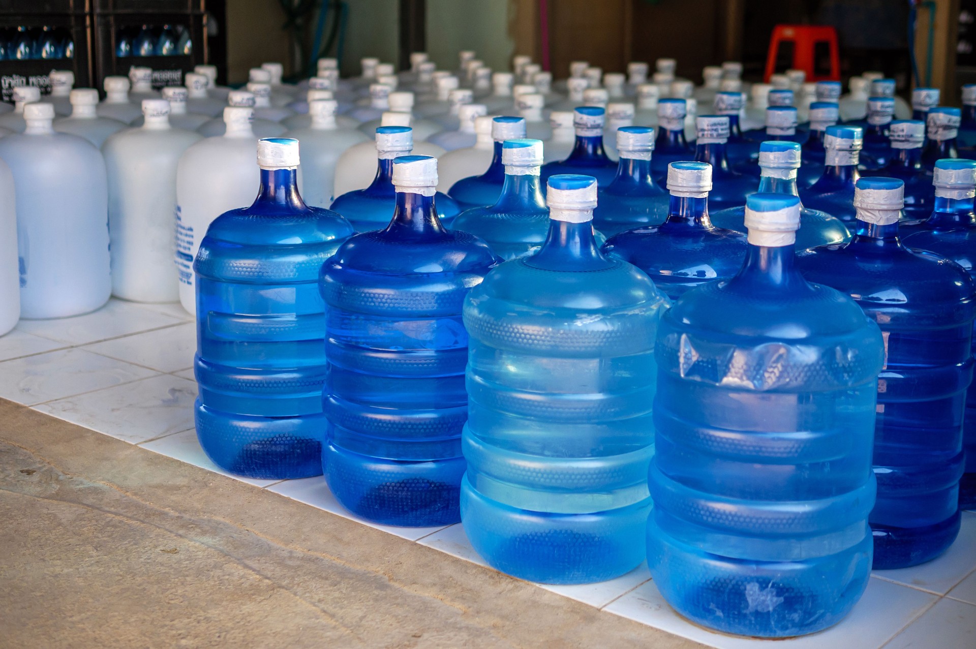Many blue gallons and white gallon of drinking water are lined up in a drinking water production plant.